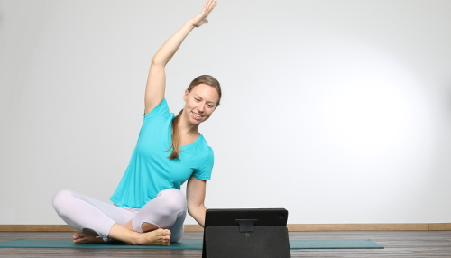 Lehrerin blickt in sitzender Seitbeuge auf Bildschirm - Yoga Gutschein erhältlich