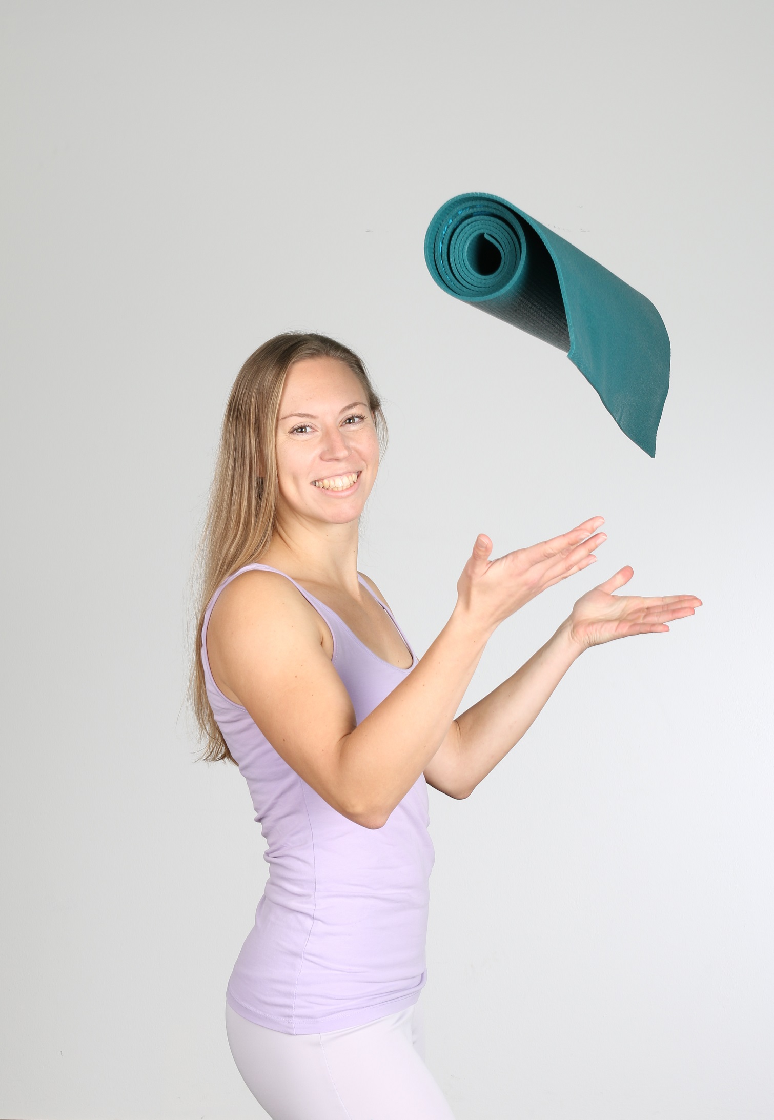 Frau in fliederfarbenem Outfit wirft lächelnd eine Yogamatte in die Luft