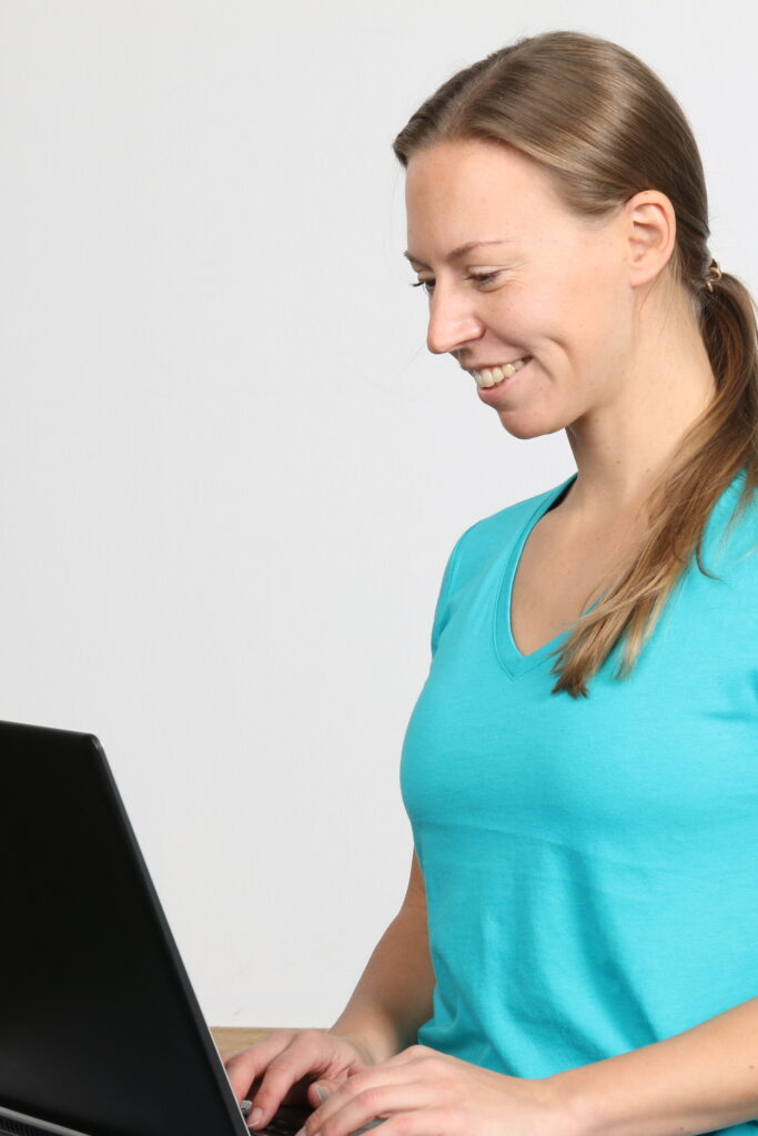 Lächelnde Frau tippt auf Laptop, welche Yoga Angebote sie aktuell plant