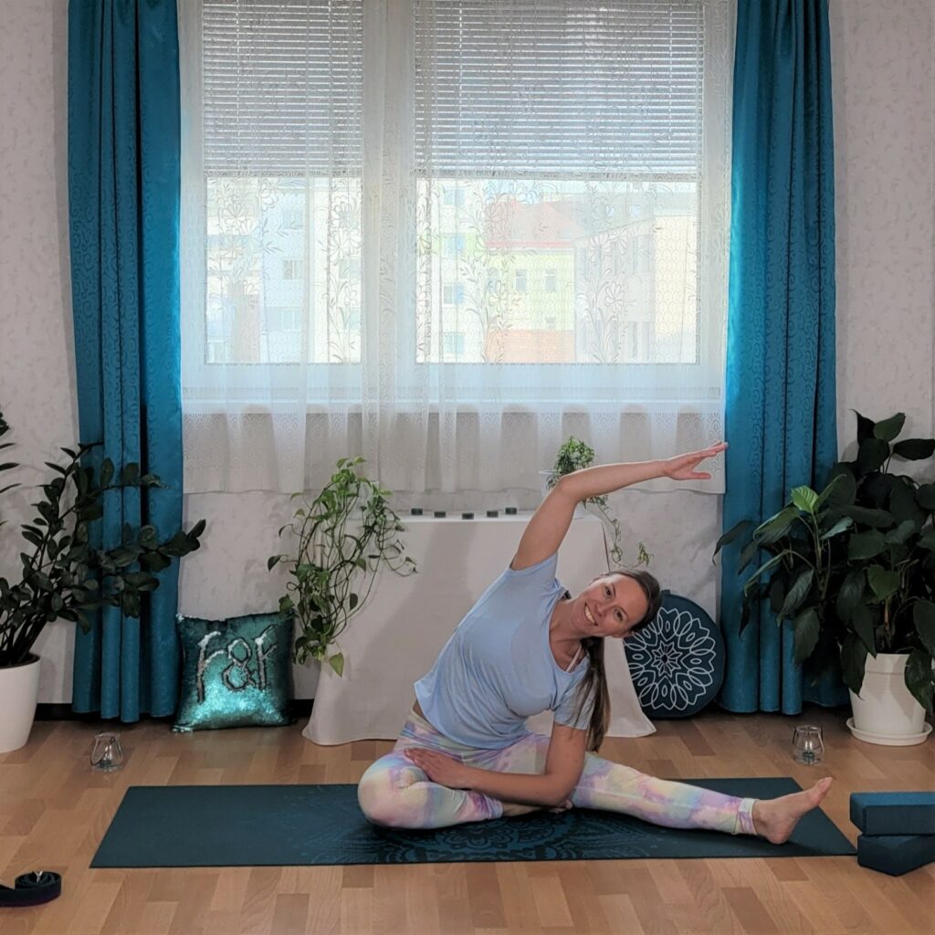 Lächelnde Yogalehrerin neigt den Oberkörper im Sitzen zur Seite, um mit Yoga ihre Müdigkeit zu bekämpfen