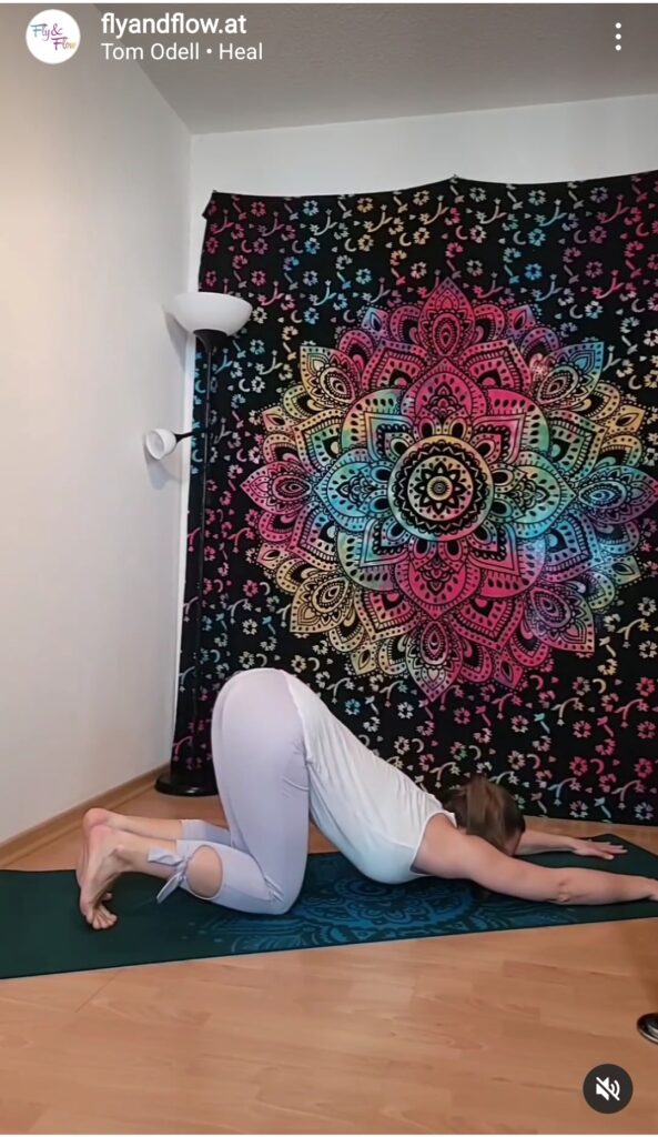 Instagram Reel Screenshot einer Frau in der Position Schmelzendes Herz vor buntem Mandala auf Wand