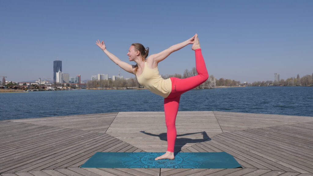 Yogalehrerin übt die Tänzer Pose auf einem Steg an der Alten Donau