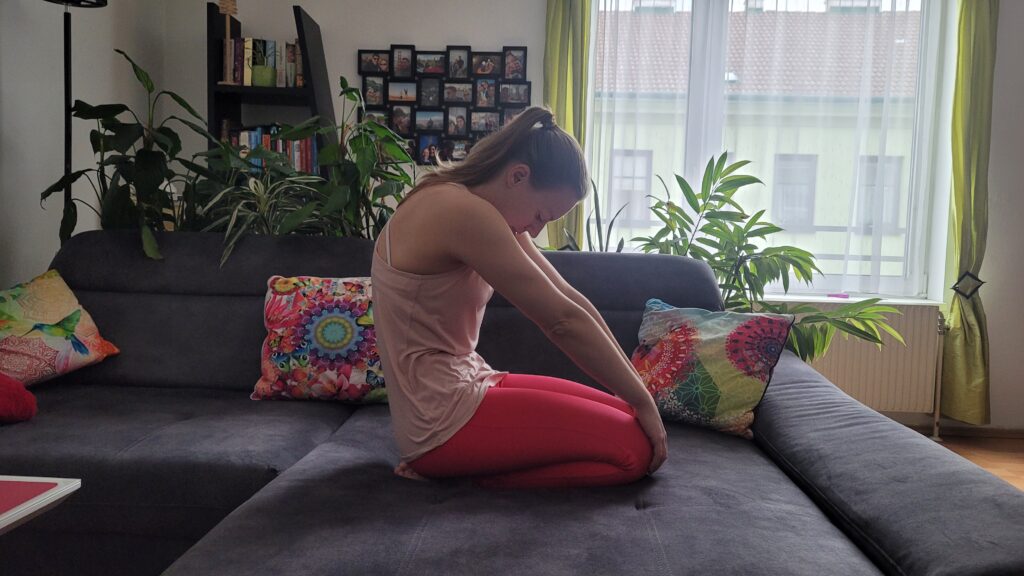 Frau im Knien auf Couch rundet ihren Rücken