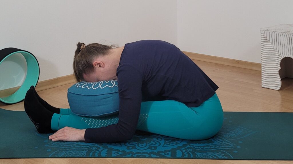 Frau in sitzender Vorbeuge mit Kopf auf Yogabolster