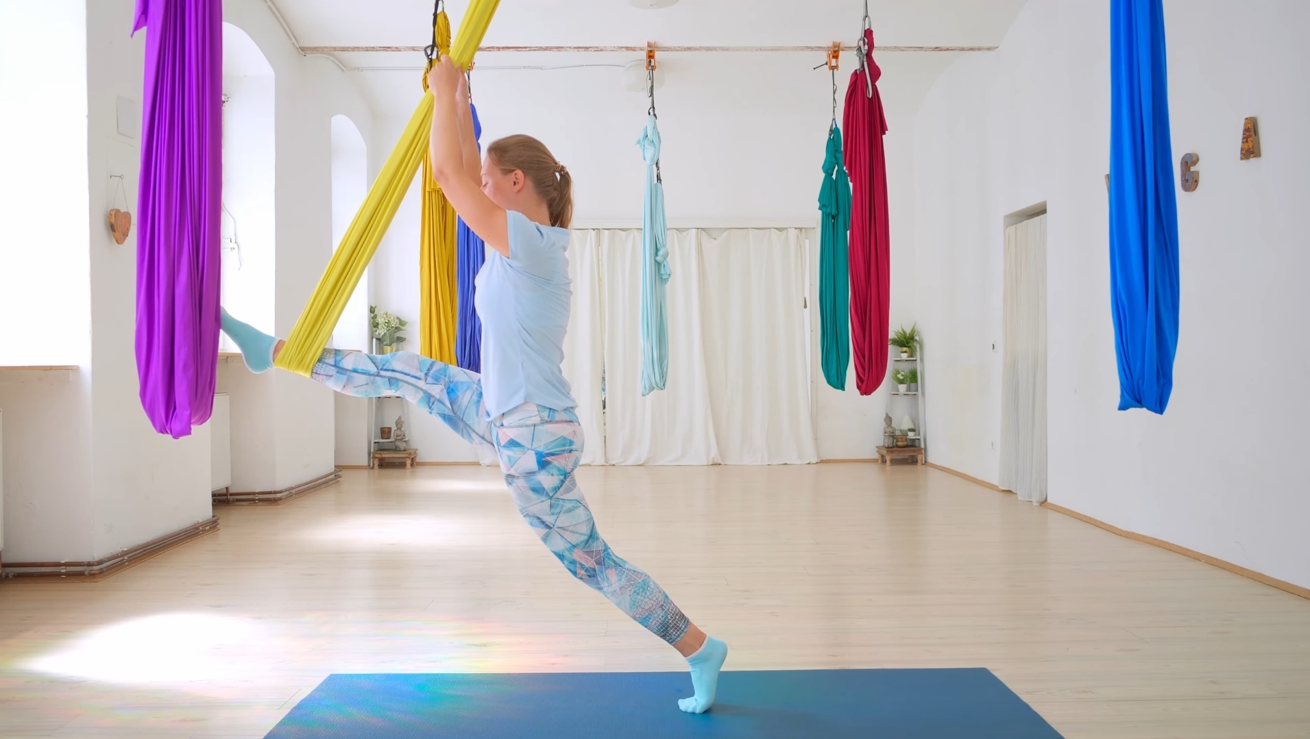 Frau zeigt Aerial Yoga Übungen in einem Studio in Wien, hier den stehenden Spagat