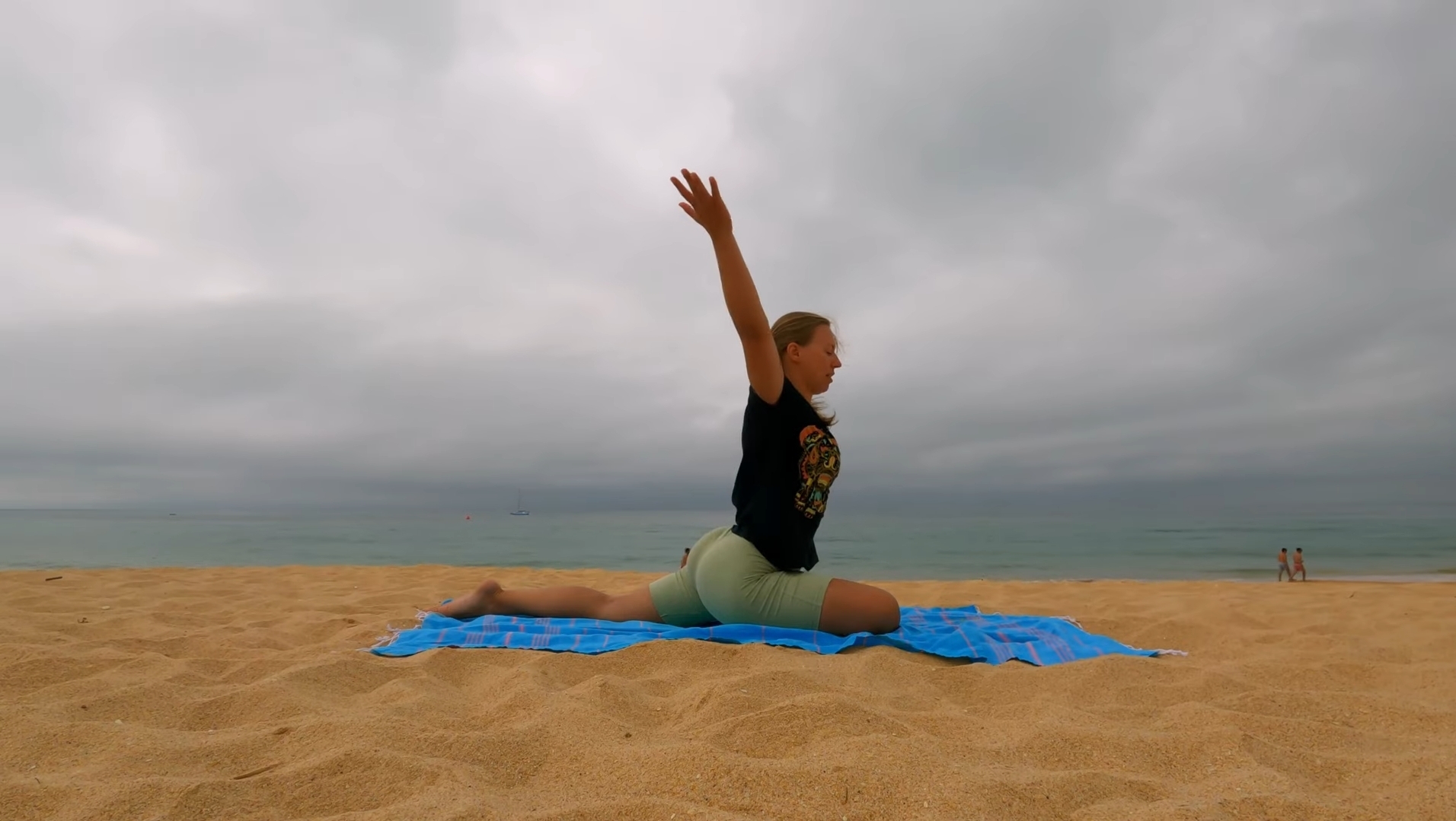 Lehrerin in der Taube beim Yoga am Sandstrand bei bewölktem Himmel und leichten Wellen
