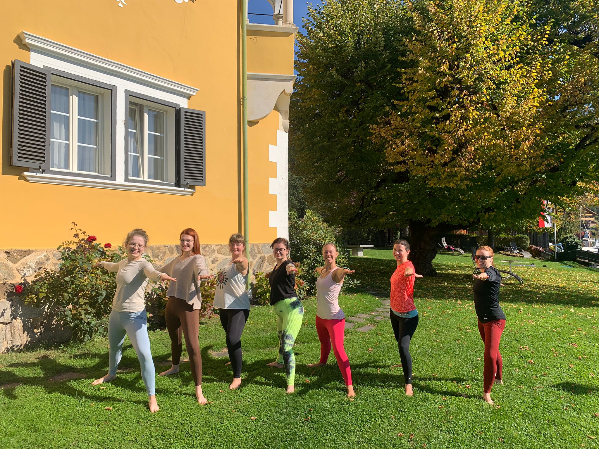Sieben Teilnehmerinnen des Yoga Retreats im Herbst üben auf einer Wiese