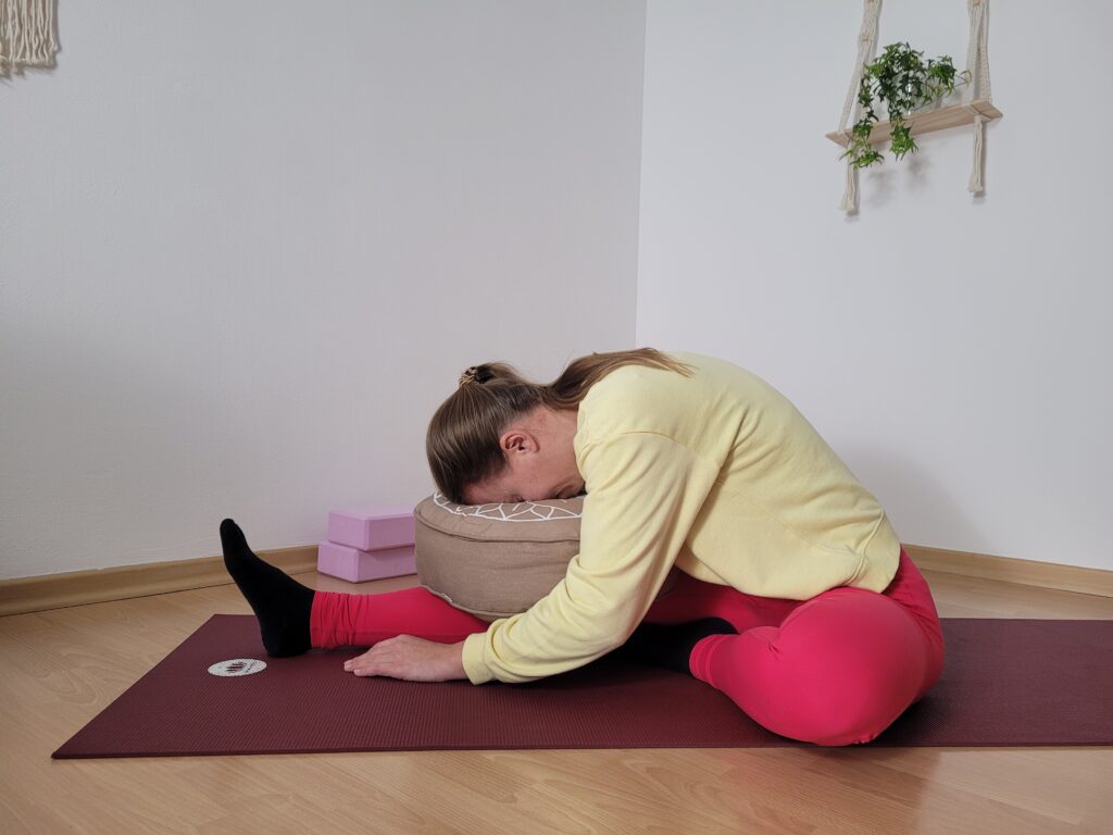 Sitz mit einem gebeugten und einem gestreckten Bein, das Gesicht auf einem Yin Yogabolster
