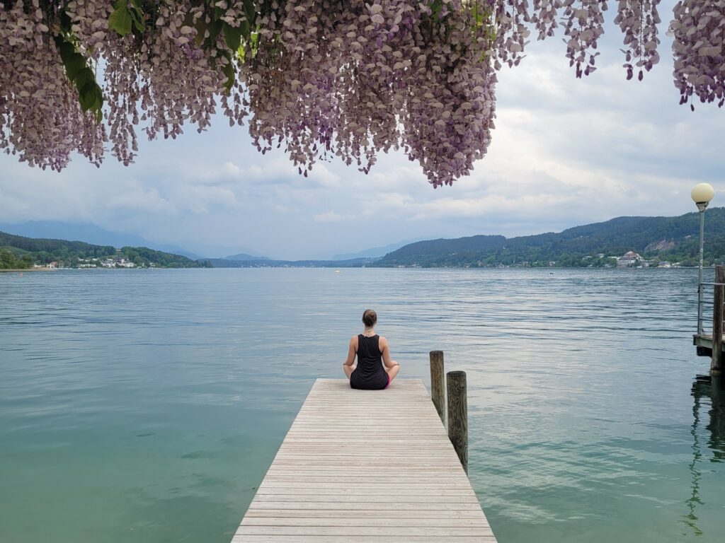 Frau im Meditationssitz auf einem Steg am See