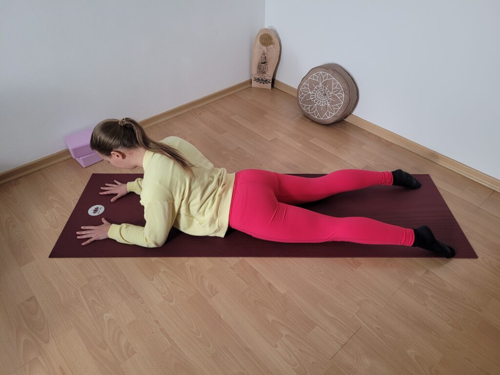 Frau in Yogakleidung auf Matte in Bauchlage mit aufgestützten Unterarmen