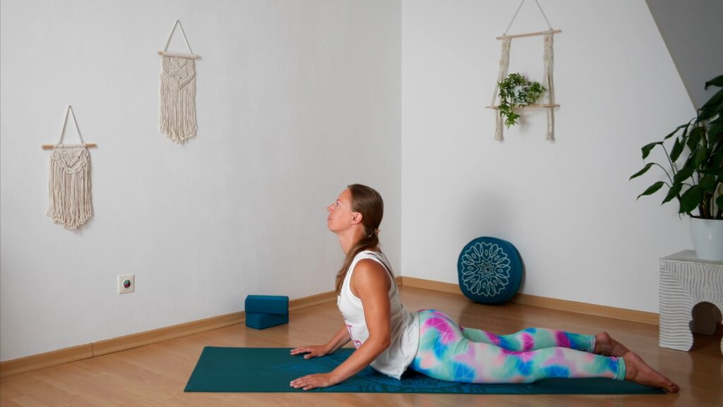 Beinvorderseite und Becken auf der Matte, die Hände aufgestützt kräftigt und dehnt den Rücken der Yogalehrerin