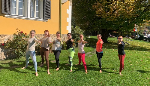 Sieben Frauen im Yoga Outfit üben auf einer Wiese beim Retreat im Herbst