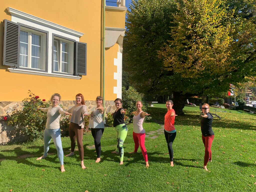 Yoga Schülerinnen und Lehrerin posieren im Krieger 2 auf der Wiese beim Yoga Retreat in Kärnten