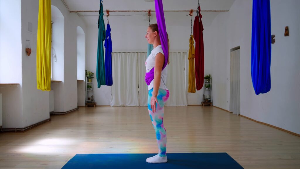 Frau im aktiven Stand, das Aerial Yoga Tuch um den Oberkörper geschlungen