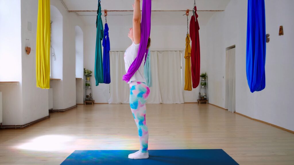 Stehende Frau mit erhobenen Armen im Aerial Yoga Tuch