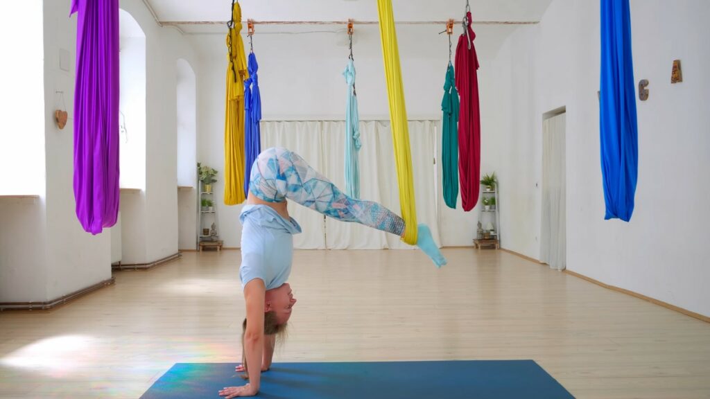 Yogini auf Hände gestützt, die Hüfte über dem Kopf, die Beine im gelben Tuch im Aerial Yoga Studio in Wien