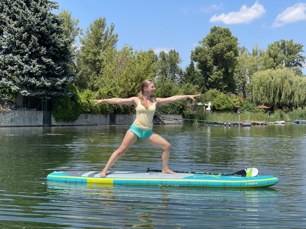 Frau in Krieger zwei Position beim SUP Yoga auf einem Fanatic Board auf der Alten Donau in Wien