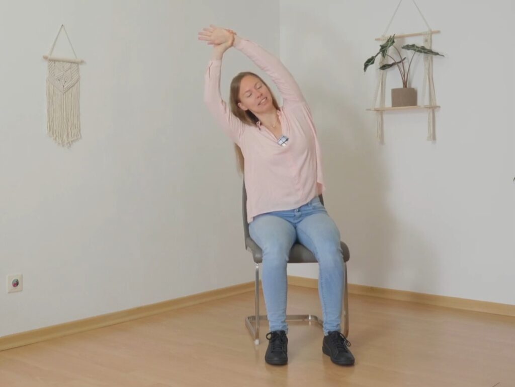 Frau beugt sich im Sitzen mit Armen über Kopf zur Seite beim Yoga im Büro