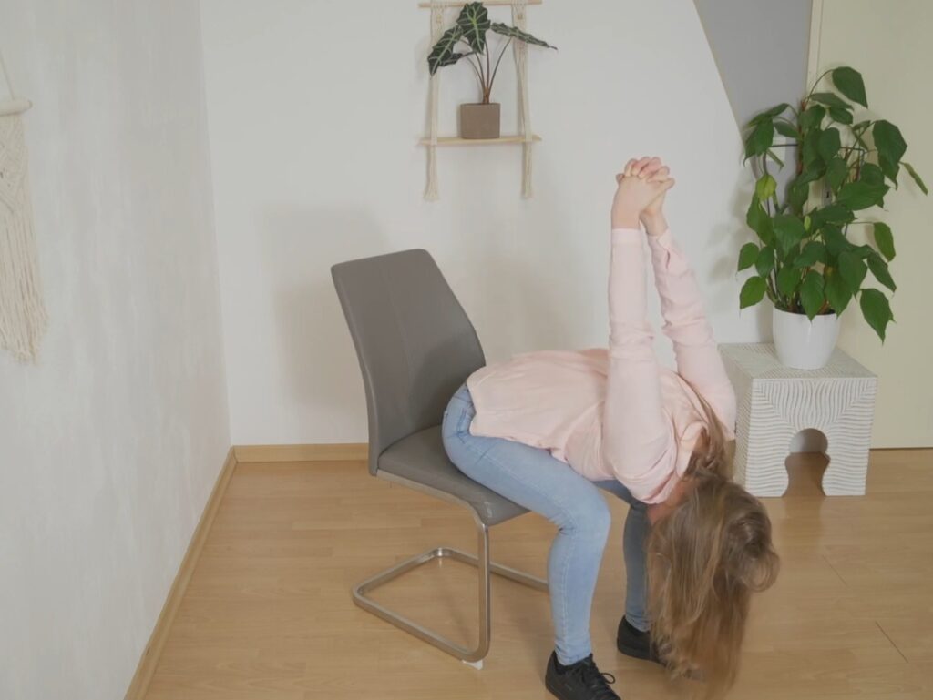 Frau beim Yoga im Büro auf Sessel in vorgebeugter Haltung mit verschränkten Händen