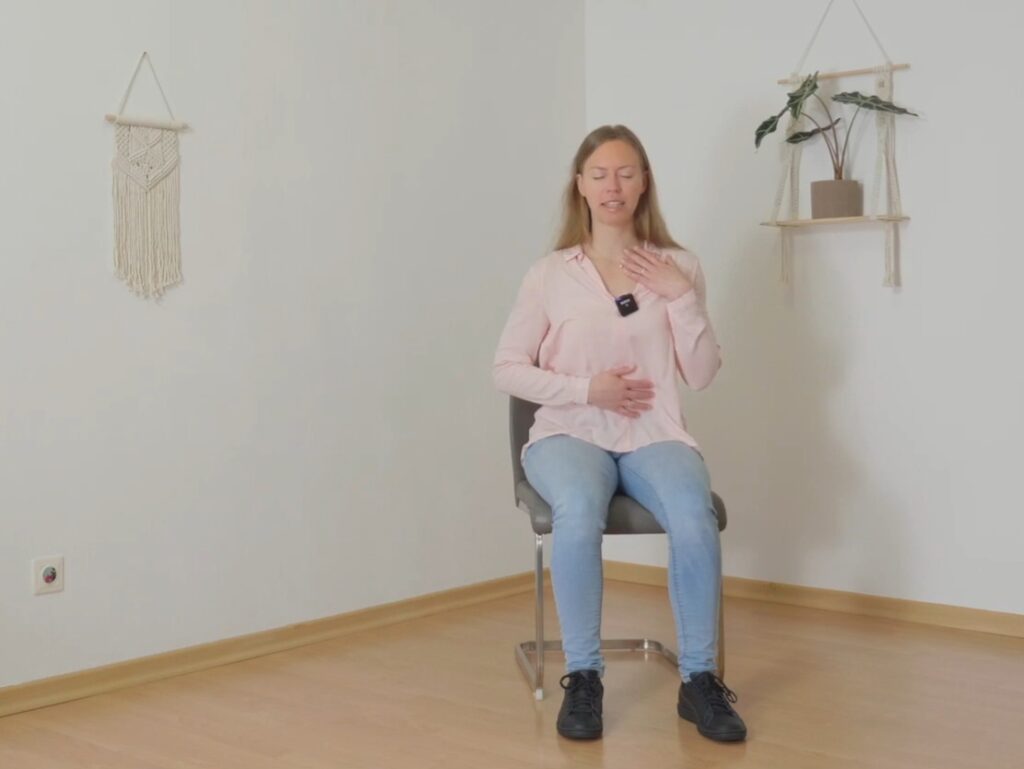 Frau auf Stuhl mit einer Hand am Herzen und einer am Bauch zu Beginn des Yoga im Büro