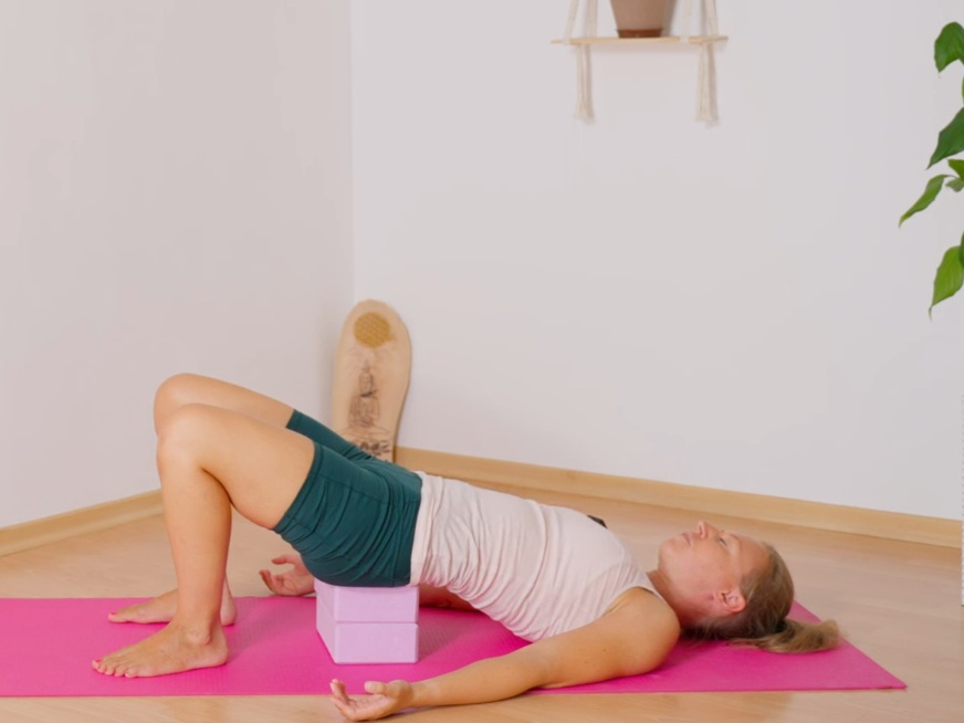 Frau in Schulterbrücke mit Yogablöcken beim Hatha Yoga für eine gesunde Haltung