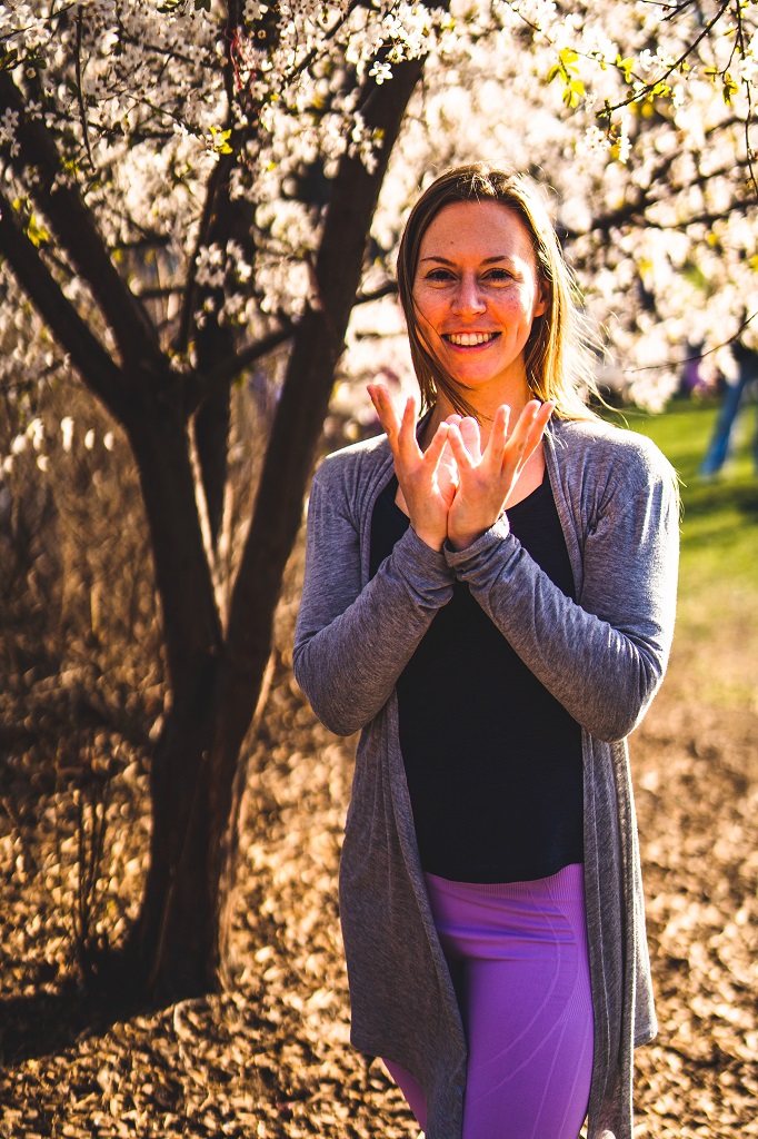 Lächelnde Frau vor blühendem Baum bildet mit ihren Händen das Lotus Mudra beim Yoga Retreat im März