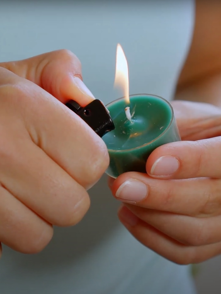 Frauenhände zünden petrolfarbenes Teelicht mit Feuerzeug an fürs Online Yoga Retreat