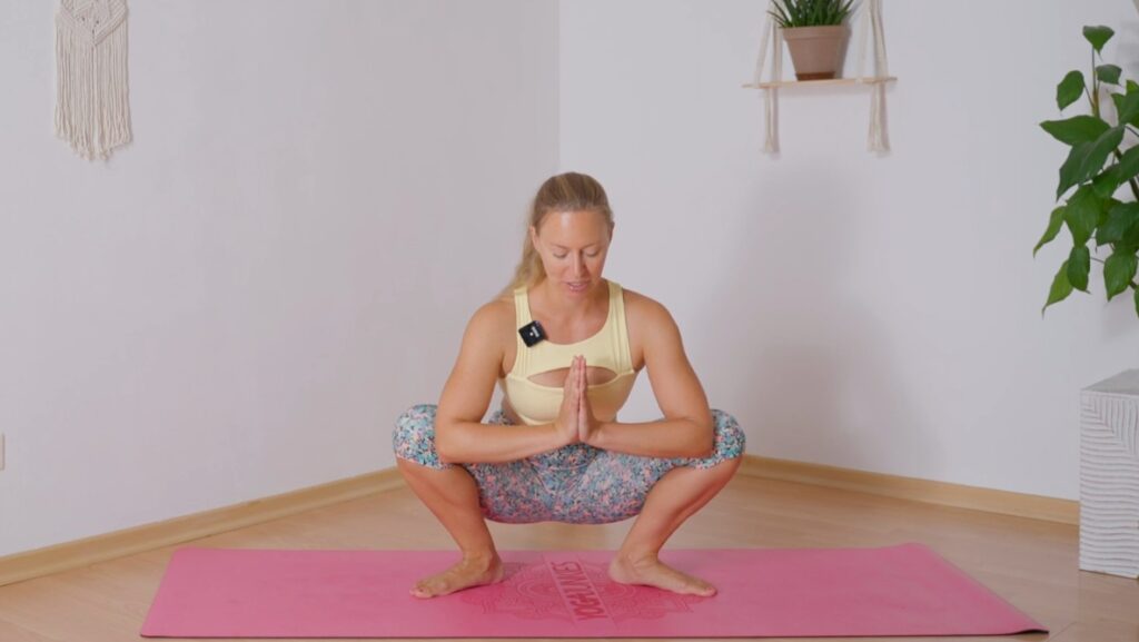 Sommerlich gekleidete Yogalehrerin in Hocke auf Yoga Junkies Matte