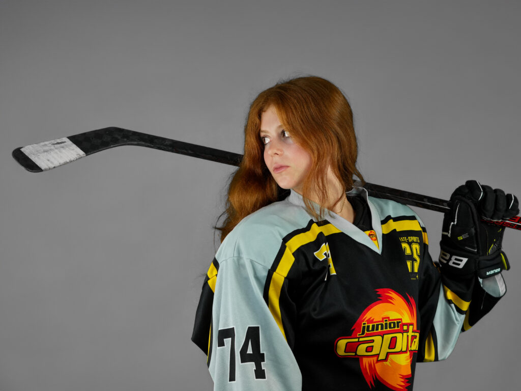 Rothaarige Junior Eishockeyspielerin mit Blick zum geschulterten Schläger