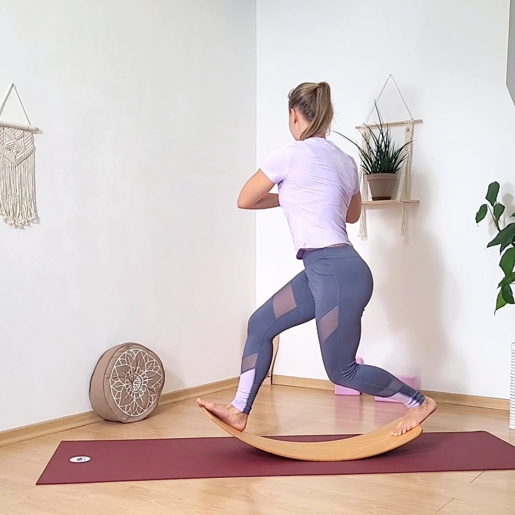 Yogalehrerin demonstriert den Twist im Ausfallschritt auf dem Yogabrett stehend