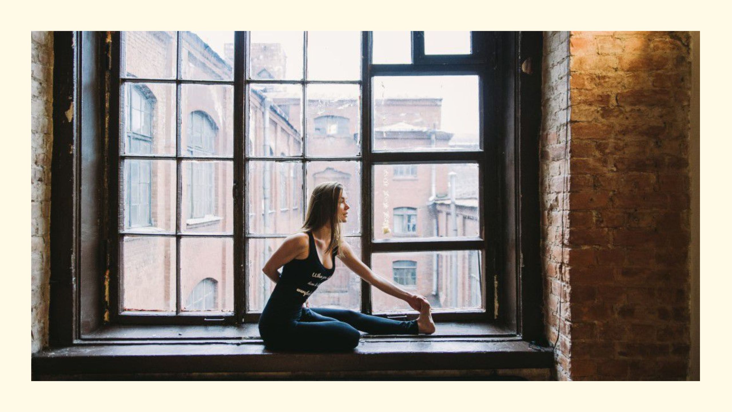 Frau in sitzender Yoga-Pose auf der Fensterbank in einem Backsteingebäude als Sinnbild für Yoga-Philosophie im Alltag