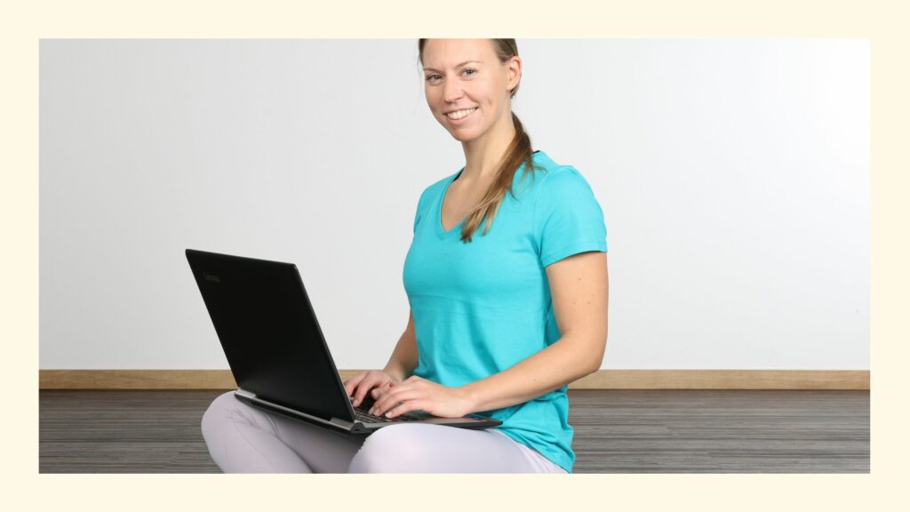 Sabrina, im Hauptberuf Yogalehrer, sitzt lächelnd mit Laptop am Schoß beim Yoga Business Training