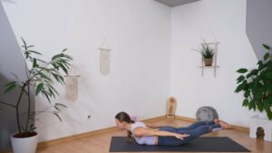 Yogalehrerin in Bauchlage mit abgehobenen Beinen und Oberkörper zur Kräftigung der Körperrückseite für Läufer