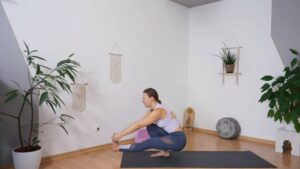 Yogalehrerin in einbeiniger Kniebeuge mit Händen am Fuß des schwebenden, gestreckten Beins