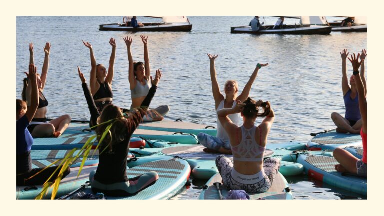 Sabrina mit ihren SUP Yoga Schülerinnen auf den Boards sitzend mit ausgestreckten Armen in Wien 2025, im Hintergrund Segelboote