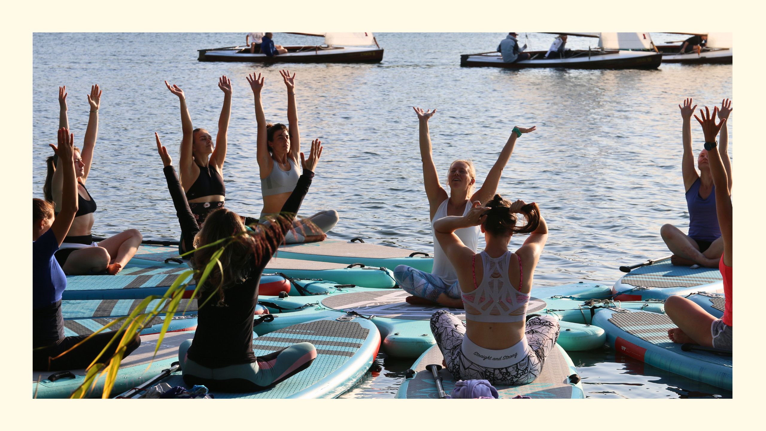 Sabrina mit ihren SUP Yoga Schülerinnen auf den Boards sitzend mit ausgestreckten Armen in Wien 2025, im Hintergrund Segelboote