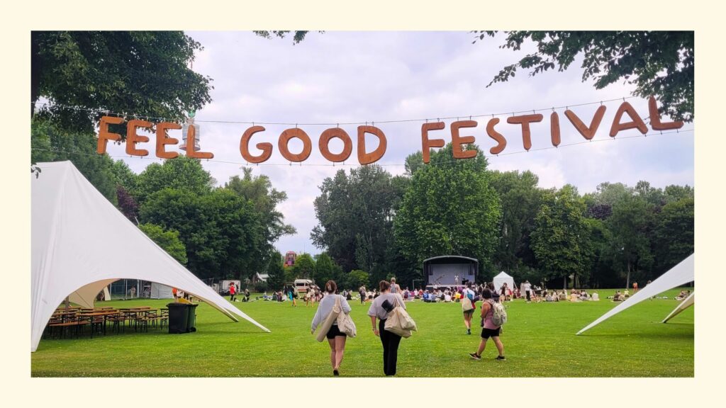 Feel Good Festival Banner im Sportcenter Donaucity mit dahinter liegender Bühne, Besucherinnen und Zelten auf grüner Wiese
