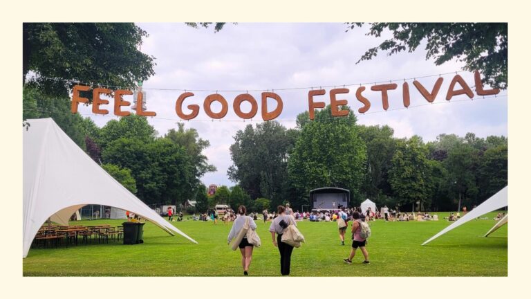 Feel Good Festival Banner im Sportcenter Donaucity mit dahinter liegender Bühne, Besucherinnen und Zelten auf grüner Wiese