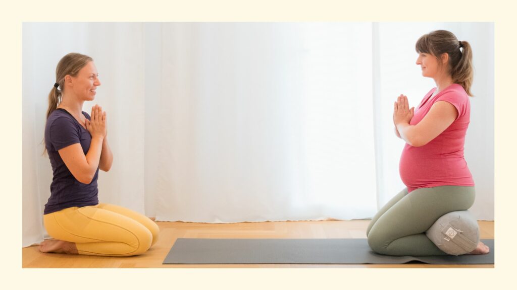 Schwangere Schülerin auf Yogamatte mit Bolster, Lehrerin Sabrina lächelnd im Knien vor ihr erklärt worauf bei Schwangerschaft im Yoga zu achten ist