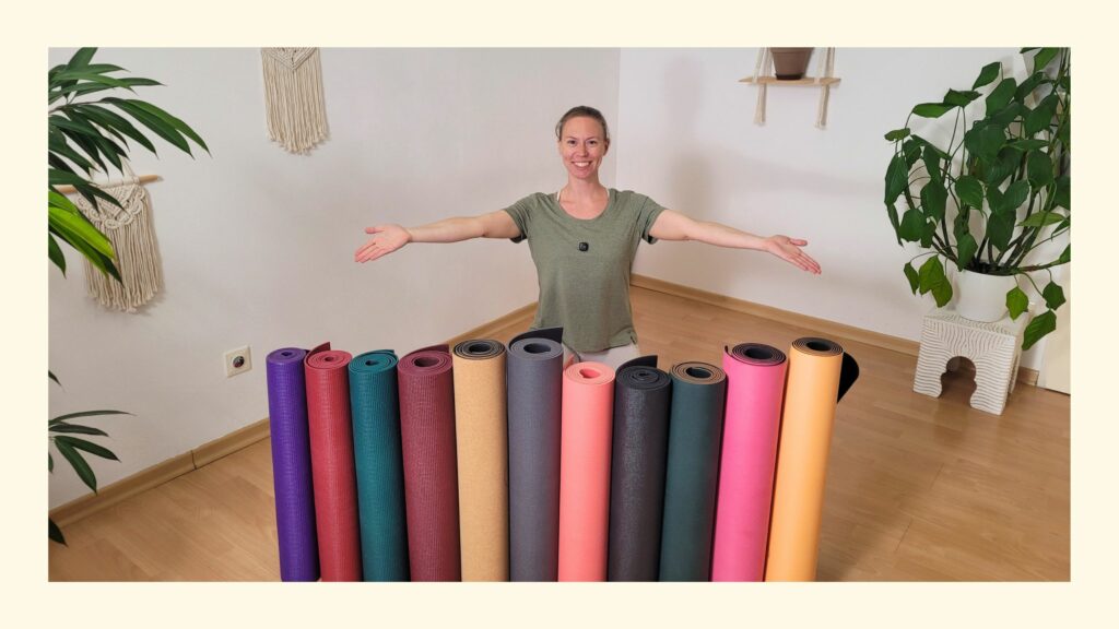Sabrina hockend in ihrem Home Studio hinter einer Reihe aufgestellter, eingerollter bunter Yogamatten beim Test, welche die beste Yogamatte 2026 ist
