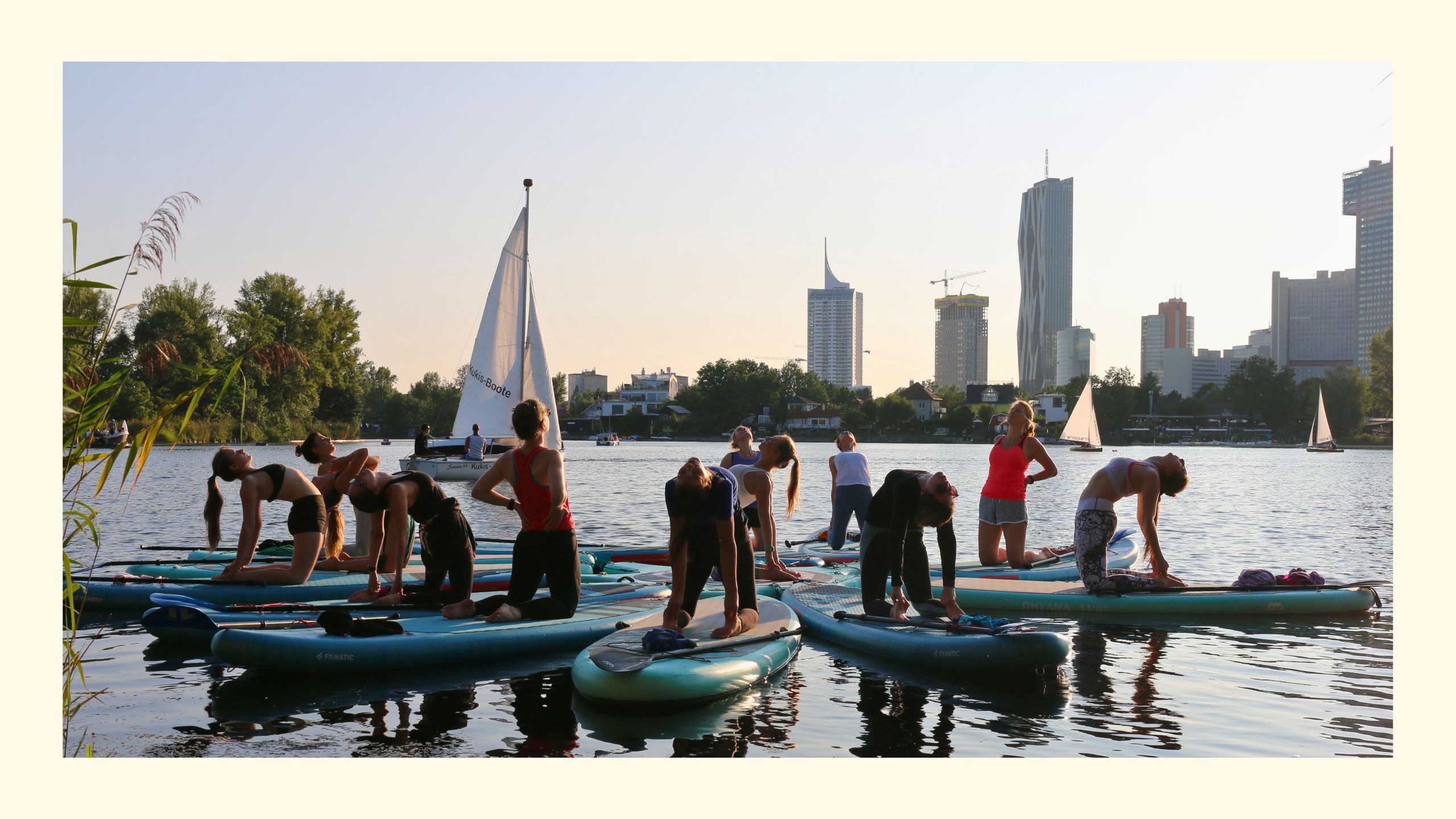 Gruppe Frauen in Kamelposition bei SUP Yoga Stunde auf der Alten Donau in Wien, unweit von Flotus und Hofbauer