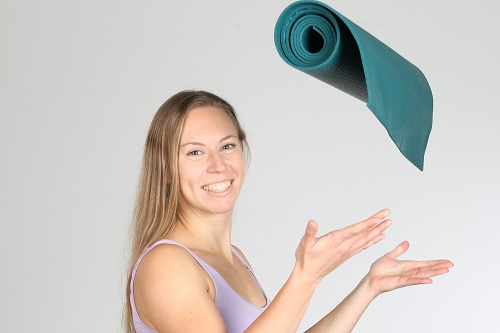 Yogalehrerin Sabrina Farkas wirft lächelnd eine zusammengerollte Yogamatte in die Luft