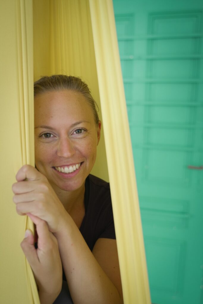 Ausbildungsleiterin Sabrina Farkas lächelt aus einem Aerial Yoga Tuch