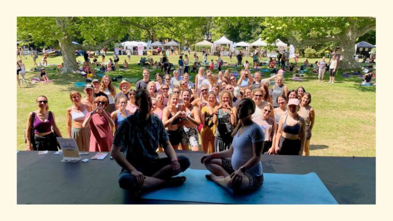 Sabrina von Fly & Flow mit Gitarrist Philipp sitzend auf der Hauptbühne des Yoga Junkies Festivals 2026 mit lächelnden Teilnehmenden im Hintergrund